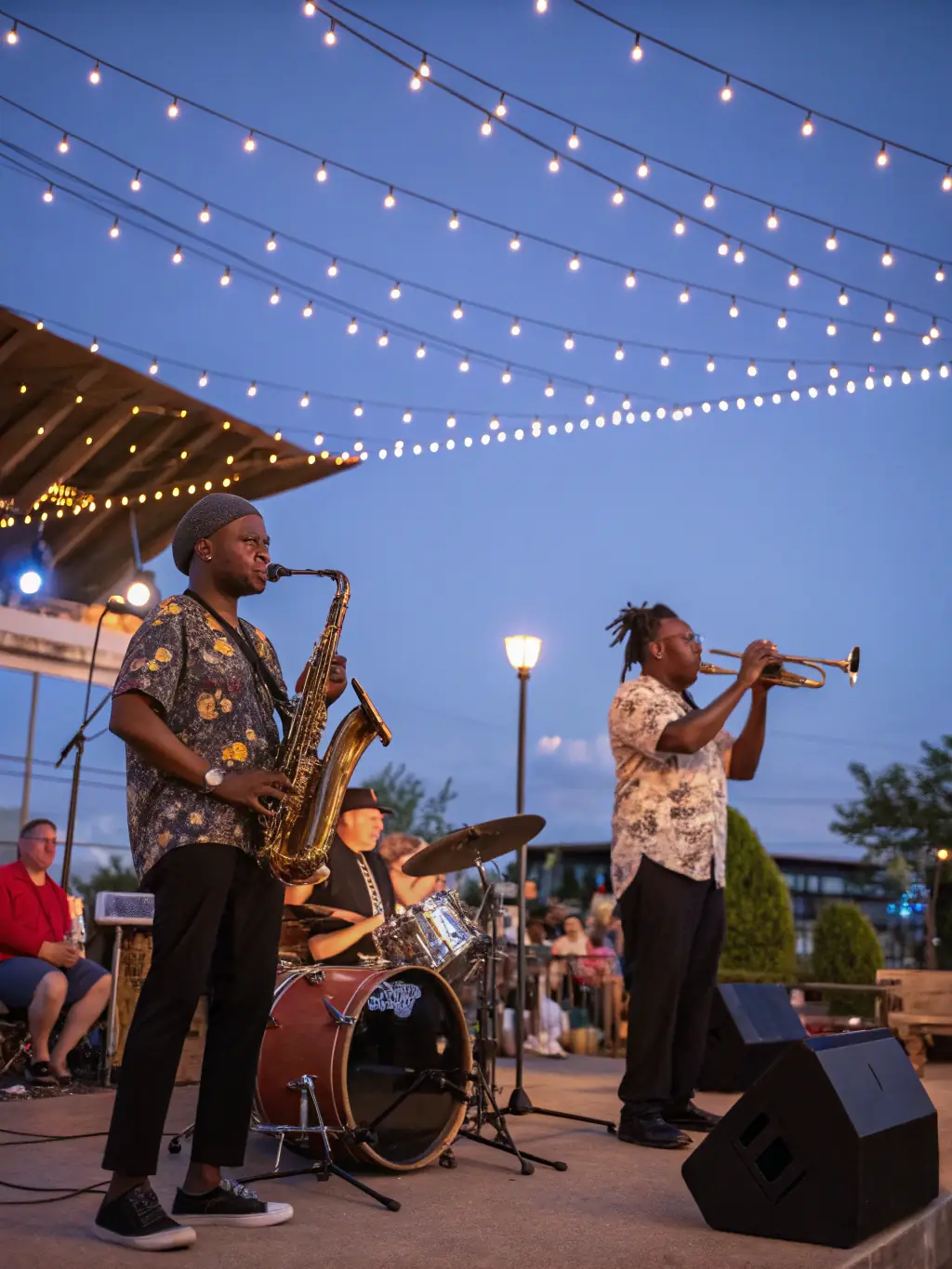 A vibrant photograph capturing a live music performance organized by BLACK HATS, showcasing a diverse group of musicians and an enthusiastic audience in a community setting.